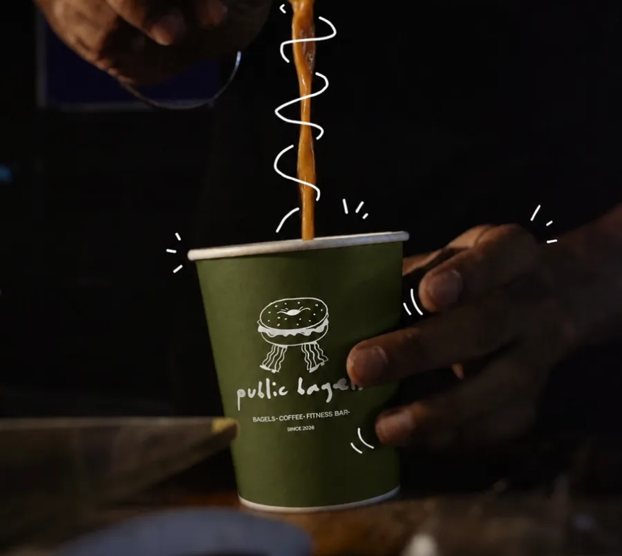 Barista de Public Bagels, bagelería en San Miguel de Allende, sirviendo café en un vaso con su logo